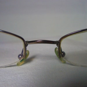 May include: A pair of silver-toned eyeglasses with clear lenses and green plastic earpieces.