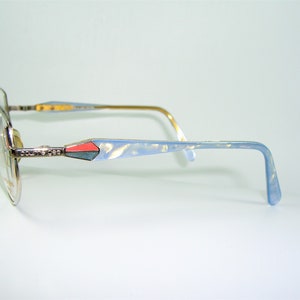 May include: Silver and blue eyeglasses with a light blue and pink accent on the temple arms. The brand name "Couture Eyes" is visible on the temple arm.