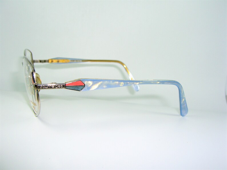 May include: Silver and blue eyeglasses with a light blue and pink accent on the temple arms. The brand name "Couture Eyes" is visible on the temple arm.