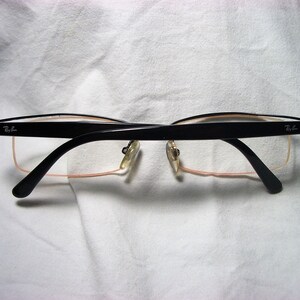 May include: Black rectangular eyeglasses with a thin metal frame and clear lenses. The brand name "Ray-Ban" is visible on the right temple.