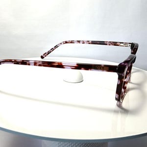 Peut inclure: Lunettes &agrave; motif &eacute;caille de tortue marron et blanc. Les montures sont de forme rectangulaire avec un l&eacute;ger design &oelig;il de chat. Les lunettes sont pr&eacute;sent&eacute;es sur une surface blanche.