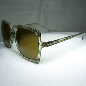 Może przedstawiać: Okulary przeciwsłoneczne w stylu vintage, duże, kwadratowe, z jasnobrązową oprawką i brązowymi szkłami.