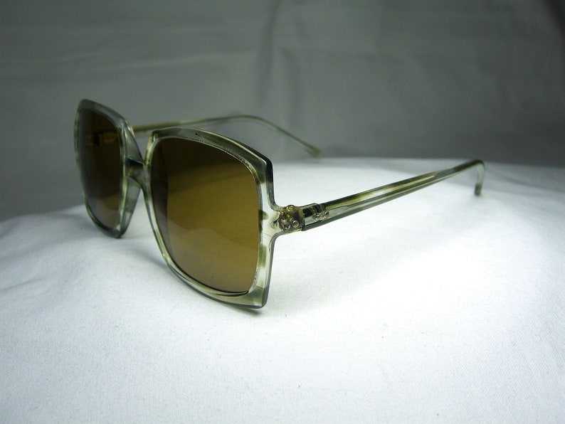 Może przedstawiać: Okulary przeciwsłoneczne w stylu vintage, duże, kwadratowe, z jasnobrązową oprawką i brązowymi szkłami.