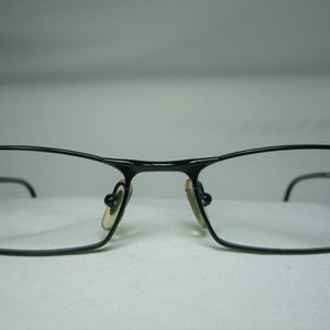 Puede incluir: Gafas rectangulares negras con finos marcos de metal.