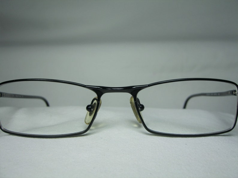 Puede incluir: Gafas rectangulares negras con finos marcos de metal.