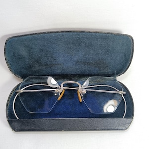 Puede incluir: Gafas plateadas con lentes transparentes en un estuche de terciopelo negro.