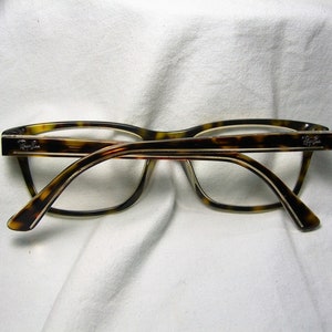 May include: Tortoise shell eyeglasses with a thin gold frame and clear lenses. The brand name "Ray-Ban" is visible on the right temple.