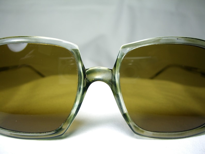 Może przedstawiać: Okulary przeciwsłoneczne vintage z jasnobrązową oprawką i brązowymi szkłami. Oprawka wykonana jest z przezroczystego plastiku i ma kwadratowy kształt.