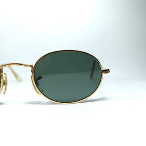 Puede incluir: Gafas de sol ovaladas con montura dorada y lentes verde oscuro.