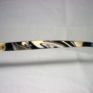 May include: Close-up of the arm of a pair of black and white tortoiseshell Ray-Ban sunglasses. The Ray-Ban logo is visible on the arm.