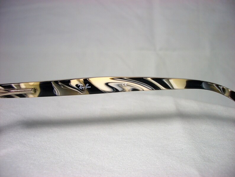 May include: Close-up of the arm of a pair of black and white tortoiseshell Ray-Ban sunglasses. The Ray-Ban logo is visible on the arm.