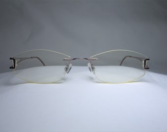 Könnte beinhalten: Eine Brille ohne Rahmen mit silbernem Gestell und klaren Gläsern. Das Gestell hat eine subtile Krümmung und ein modernes Design.