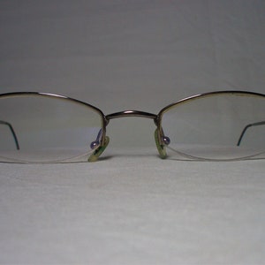 May include: A pair of silver-toned eyeglasses with a rimless design and oval-shaped lenses.