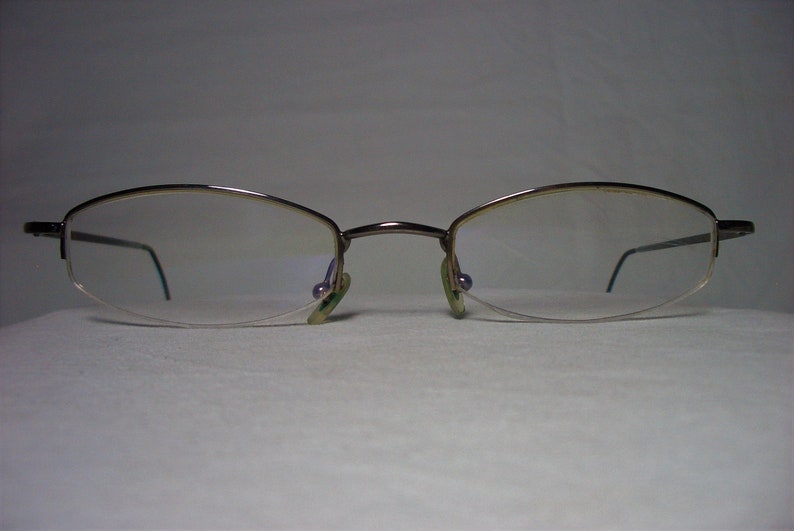 May include: A pair of silver-toned eyeglasses with a rimless design and oval-shaped lenses.