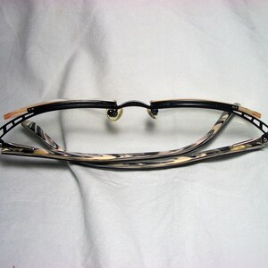 May include: Black and gold-toned eyeglasses with a tortoiseshell pattern on the arms. The glasses are folded in half.