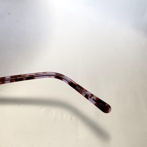 Peut inclure: Gros plan sur la branche de lunettes avec un motif &eacute;caille de tortue marron et violet. Le texte "5002540 CE" est imprim&eacute; sur la branche.