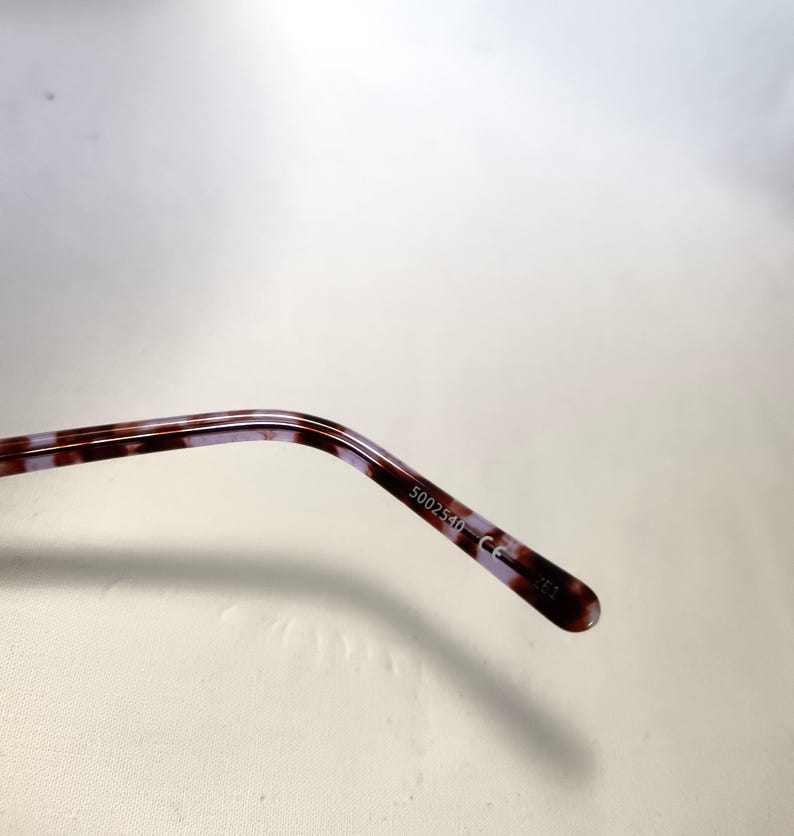 Peut inclure: Gros plan sur la branche de lunettes avec un motif &eacute;caille de tortue marron et violet. Le texte "5002540 CE" est imprim&eacute; sur la branche.