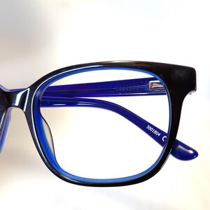 May include: Close-up of eyeglasses with a black frame and blue interior. The arms and lenses are blue. The text "5001804 C" is printed on the arm of the glasses.