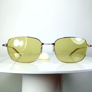 May include: A pair of eyeglasses with a thin, metallic gold frame and rectangular lenses tinted in a soft, pale yellow hue. The design features a classic bridge and slender temples, providing a clear view of the front-facing structure.