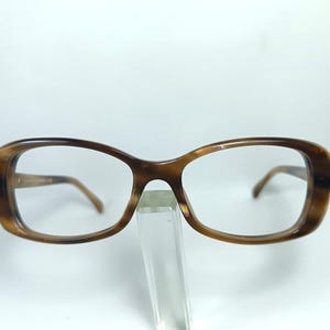 May include: Brown tortoiseshell eyeglasses with a rectangular frame. The glasses have a classic design with a subtle curve at the top of the frame. The lenses are clear, and the temples are a matching brown colour.