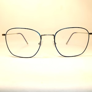May include: A pair of eyeglasses with a thin, silver-colored frame and square lenses. The rims are outlined in a dark blue color. The glasses are designed for vision correction and are suitable for everyday use.