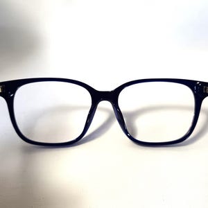 May include: A pair of dark blue rectangular eyeglasses with clear lenses. The frames are thick and have a rounded shape at the top corners. The glasses are set against a white background.