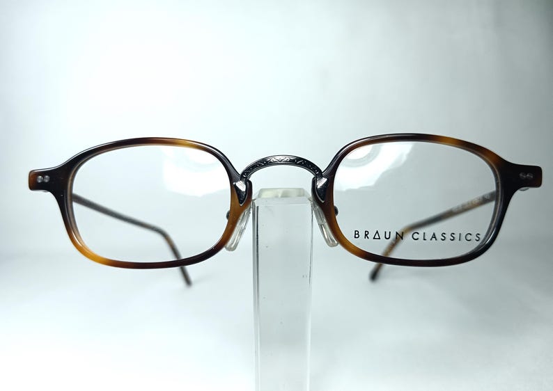 May include: Brown and black Braun Classics eyeglasses with a tortoiseshell pattern on the frames. The glasses have a metal bridge and thin temples. The brand name is printed on the right lens.