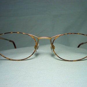 Könnte beinhalten: Eine Brille mit goldfarbenem Rahmen und Schildpatt-Akzenten. Die Brille hat ovale Gläser und einen dünnen Metallrahmen.