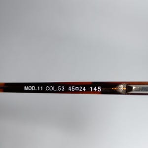 May include: Close-up of the arm of a pair of eyeglasses. The frame is a dark brown tortoiseshell pattern. The text "MOD.11 COL.53 45▢24 145" is printed in white on the arm.