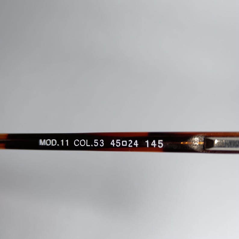 May include: Close-up of the arm of a pair of eyeglasses. The frame is a dark brown tortoiseshell pattern. The text "MOD.11 COL.53 45▢24 145" is printed in white on the arm.