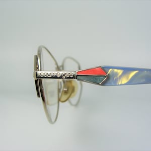May include: Silver-toned eyeglasses with a blue and red accent on the temple arm. The brand name "Courreges" is engraved on the arm.