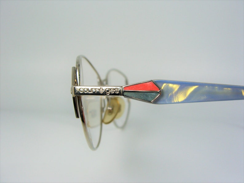 May include: Silver-toned eyeglasses with a blue and red accent on the temple arm. The brand name "Courreges" is engraved on the arm.