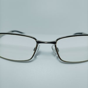 Puede incluir: Gafas con montura plateada y lentes transparentes. Las gafas tienen una forma rectangular y est&aacute;n dise&ntilde;adas para el uso diario.