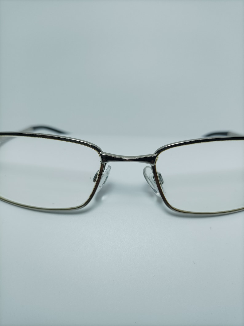 Puede incluir: Gafas con montura plateada y lentes transparentes. Las gafas tienen una forma rectangular y est&aacute;n dise&ntilde;adas para el uso diario.