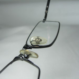Puede incluir: Gafas de metal negro con lentes transparentes y un peque&ntilde;o logotipo plateado en el lateral.