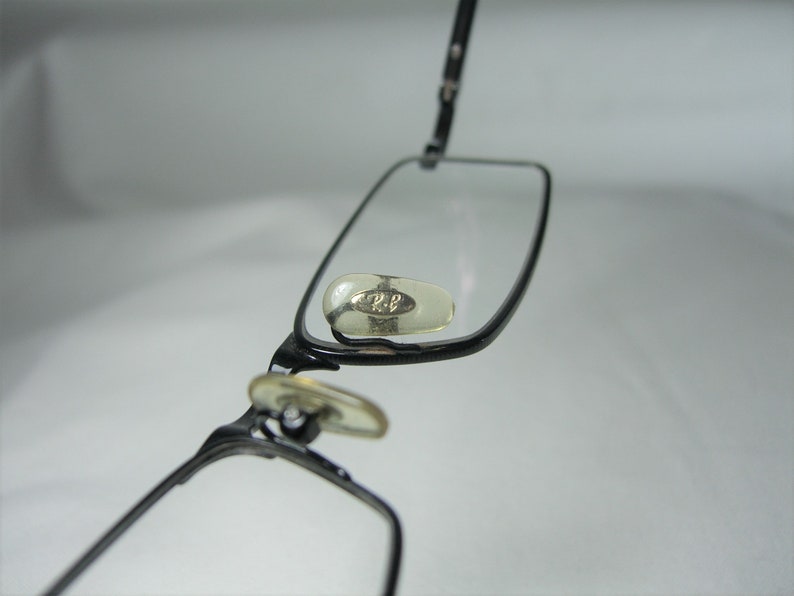 Puede incluir: Gafas de metal negro con lentes transparentes y un peque&ntilde;o logotipo plateado en el lateral.