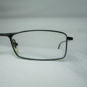 Puede incluir: Gafas rectangulares negras con finos marcos de metal y lentes transparentes.