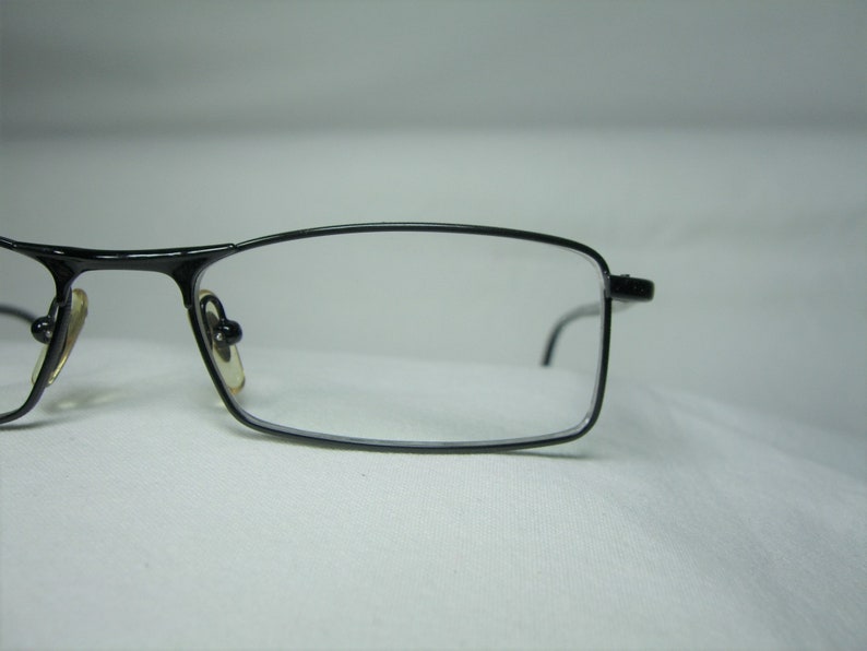 Puede incluir: Gafas rectangulares negras con finos marcos de metal y lentes transparentes.