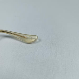 Puede incluir: Primer plano del brazo met&aacute;lico dorado de unas gafas. El brazo est&aacute; hecho de metal y tiene una punta de pl&aacute;stico transparente con el texto "5215 140A1 CE" impreso en &eacute;l.