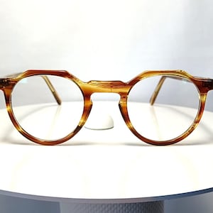 May include: Round-framed eyeglasses with a tortoise shell pattern. The glasses have a keyhole bridge and thin gold-colored arms. The lenses are clear. The glasses are set against a white background.