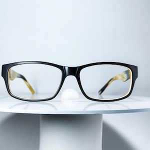 May include: Rectangular spectacles featuring a solid black frame front and clear lenses. The inner side of the frame and the temple arms display a light yellow and brown tortoiseshell pattern, providing a distinct contrast to the black exterior.