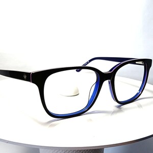 May include: Black eyeglasses with a rectangular frame and blue accents. The glasses have a sleek design with a dark frame and blue interior. The lenses are clear, and the glasses are displayed on a white surface.