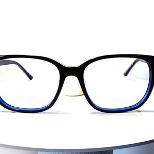 May include: Black-framed eyeglasses with a blue inner rim. The glasses have a square shape and are set against a white background. The temples are thin and have a purple hue.