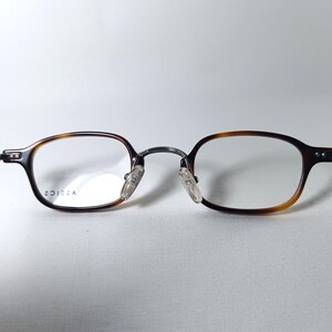 May include: Eyeglasses with a brown tortoiseshell frame and clear lenses. The glasses have a classic, rectangular shape with a metal bridge and nose pads. The frame transitions from a dark brown to a lighter amber color. The text "20122A" is printed on the lens.