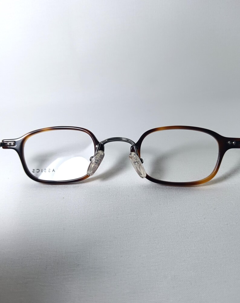 May include: Eyeglasses with a brown tortoiseshell frame and clear lenses. The glasses have a classic, rectangular shape with a metal bridge and nose pads. The frame transitions from a dark brown to a lighter amber color. The text "20122A" is printed on the lens.