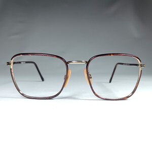 May include: A pair of tortoiseshell eyeglasses with gold accents. The glasses have a rectangular frame and clear lenses.
