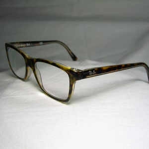 May include: Tortoise shell eyeglasses with clear lenses. The brand name "Ray-Ban" is visible on the side of the frame.