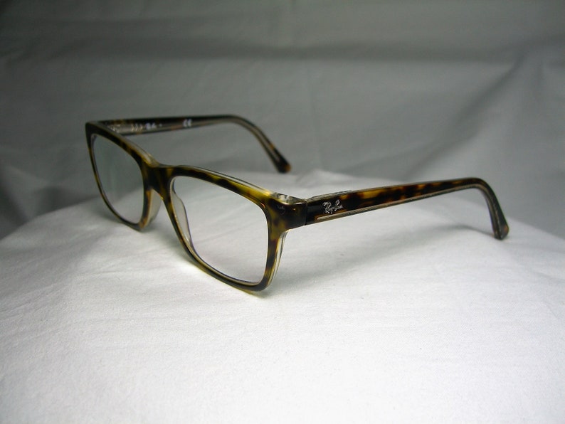 May include: Tortoise shell eyeglasses with clear lenses. The brand name "Ray-Ban" is visible on the side of the frame.