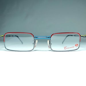 May include: A pair of eyeglasses with a red, blue, and black frame. The frame is made of metal and has a rectangular shape. The lenses are clear. The brand name "Casanova" is printed on the right lens.