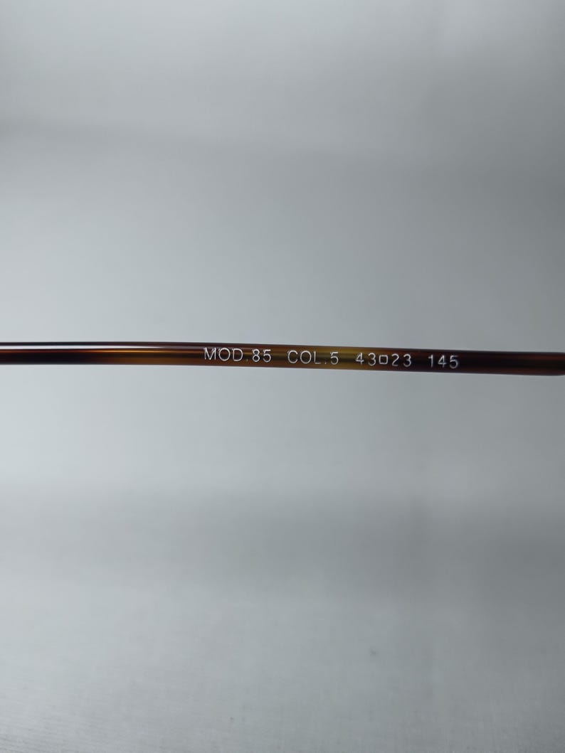 May include: Close-up of the arm of a pair of eyeglasses. The arm is a brown tortoiseshell pattern. White text on the arm reads "MOD.85 COL.5 43023 145".